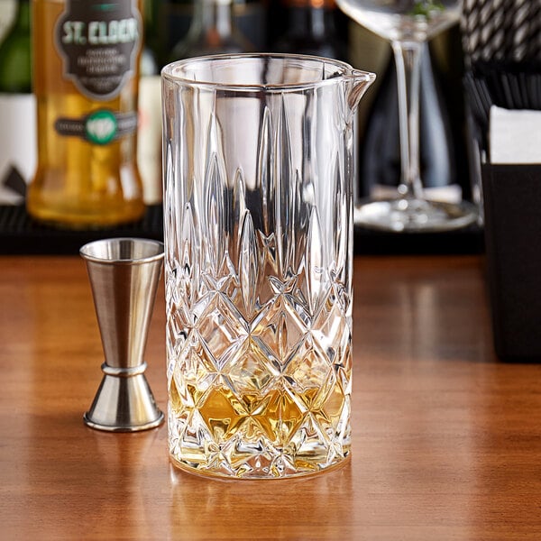A Nachtmann Noblesse stirring glass pitcher on a table with a yellow drink inside.