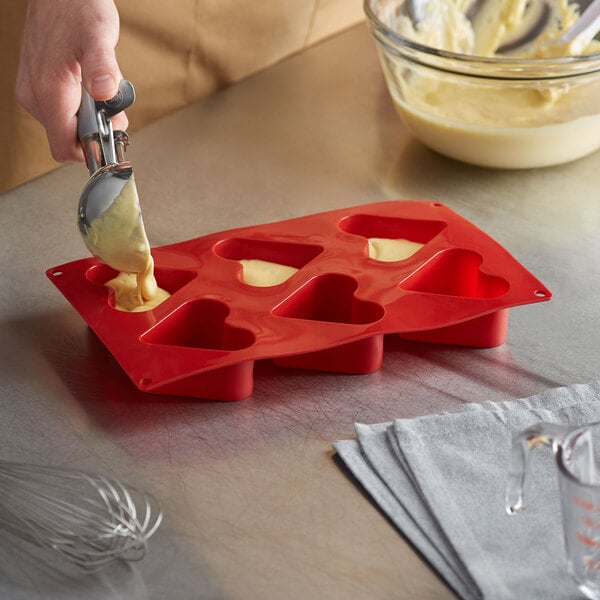A person pouring batter into a red Thunder Group heart shaped silicone mold.