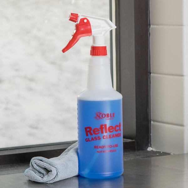 A blue and white 32 oz. spray bottle of Noble Chemical Reflect Glass / Multi-Surface Cleaner on a window sill with a red label.