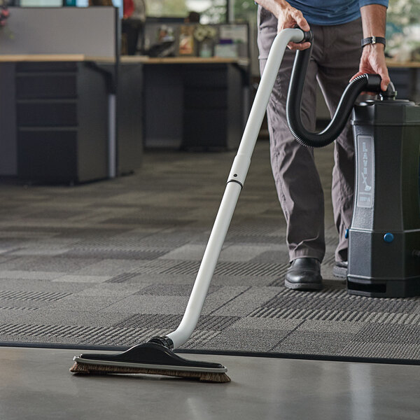 A person using a Lavex vacuum tool kit to vacuum a floor in a corporate office cafeteria.