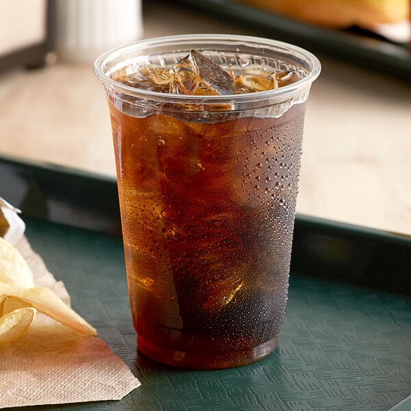 A clear Fabri-Kal plastic cup filled with iced tea on a table with ice and a napkin.