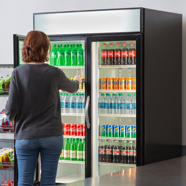 A woman standing in front of a Beverage-Air glass door merchandiser refrigerator full of beverages.