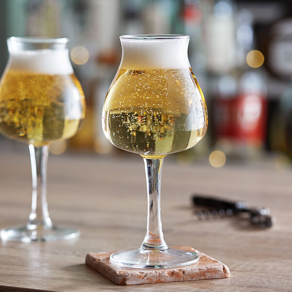 Two Libbey tall stemmed beer glasses on a wooden table.