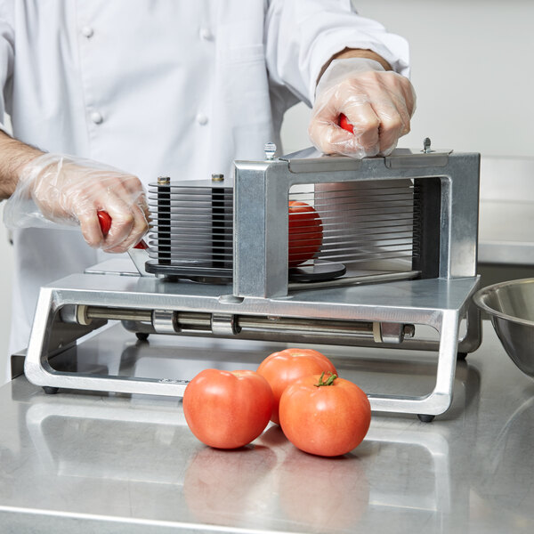 A person in gloves slicing tomatoes with a Vollrath Redco InstaSlice machine.