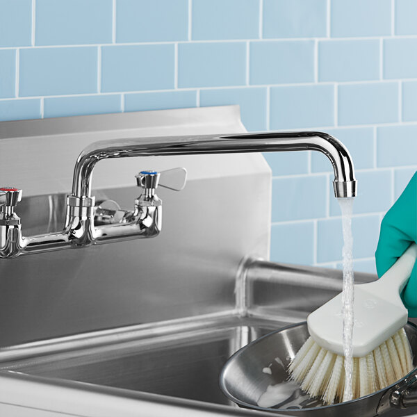 A person cleaning a sink with a 12" swing spout dish brush.