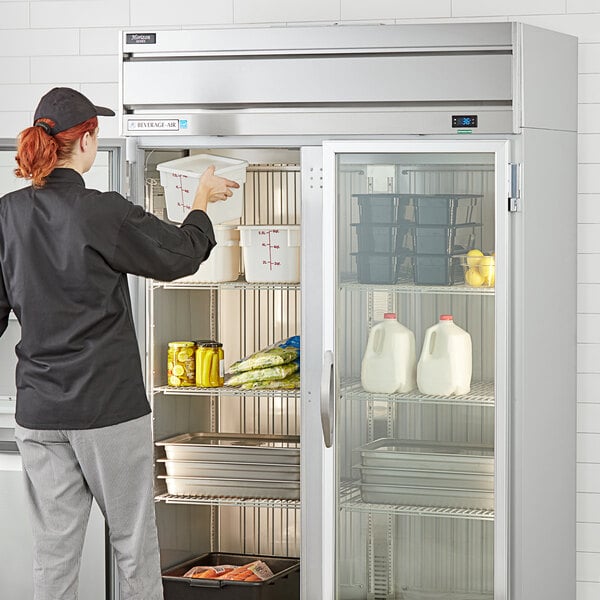 A woman opening a Beverage-Air Horizon Series glass door reach-in refrigerator in a professional kitchen.