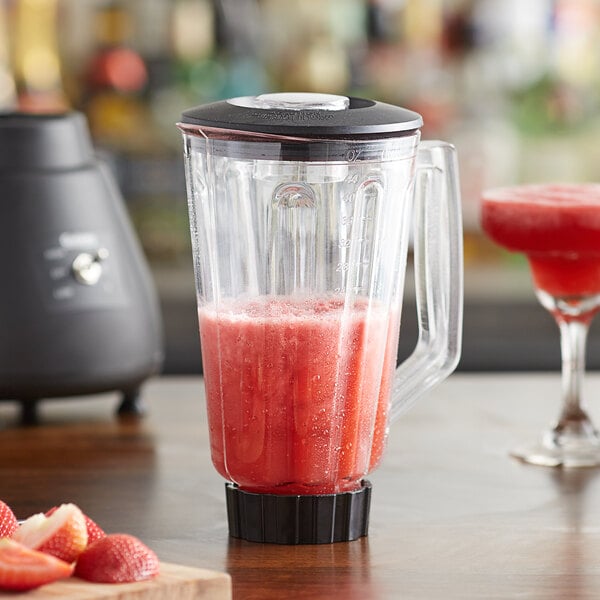 A Galaxy 44 oz. polycarbonate blender jar filled with a red drink on a table in a smoothie shop.