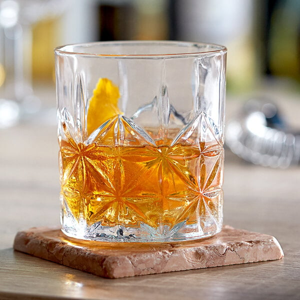 An Acopa Gardenia rocks glass with a drink and a slice of orange on a coaster.
