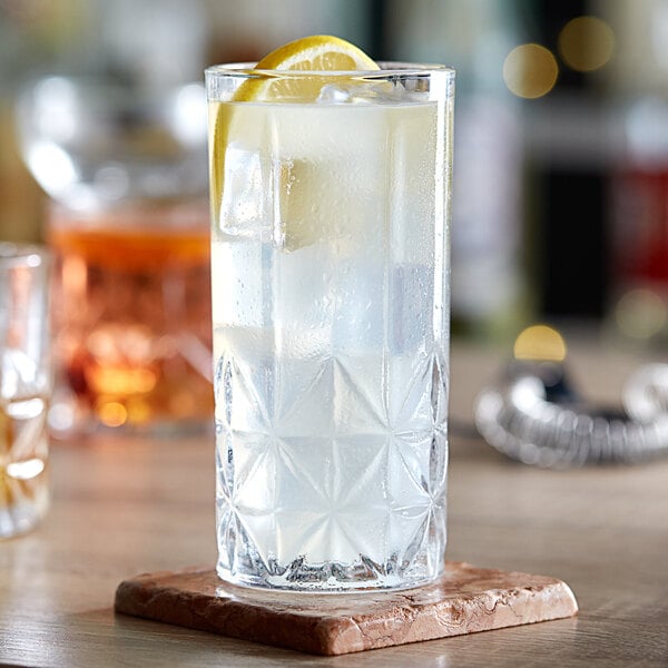 A close-up of an Acopa Gardenia highball glass of water with a lemon slice on a coaster.