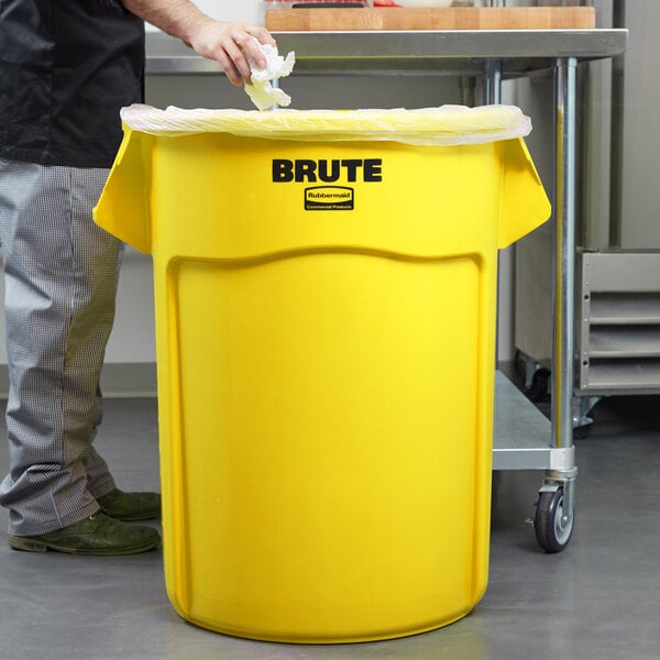 A man putting a white glove in a yellow Rubbermaid BRUTE trash can.