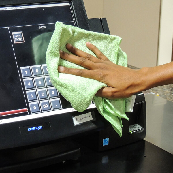 A hand wiping a cash register with a green Unger SmartColor microfiber cloth.