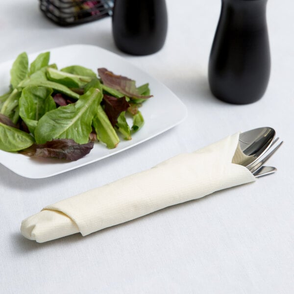 A plate of salad with a fork and spoon on an ivory linen-like napkin.