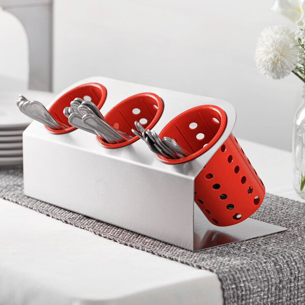 A Steril-Sil stainless steel flatware organizer with red perforated plastic cylinders holding silverware.