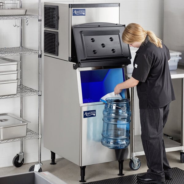 A woman standing in front of an Avantco air cooled half cube ice machine with bin.