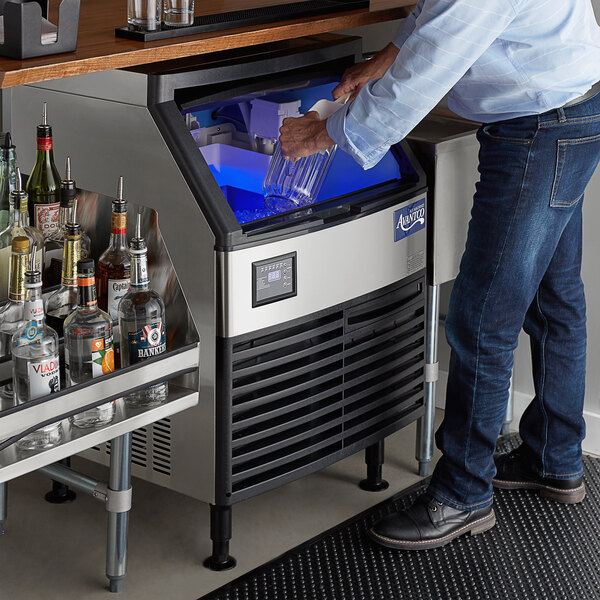 A person standing at a counter putting a glass in an Avantco undercounter ice machine.