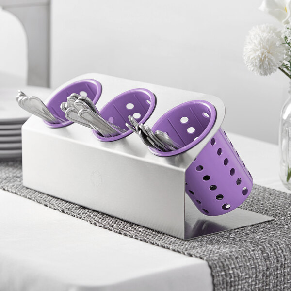 A Steril-Sil stainless steel flatware organizer with violet perforated plastic cylinders holding silverware on a table.