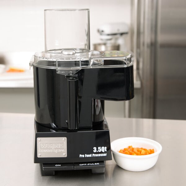 A Waring food processor with a bowl of diced carrots on top.