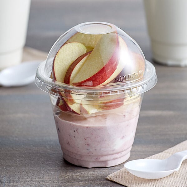 A clear plastic squat cup with apples and strawberries in it.