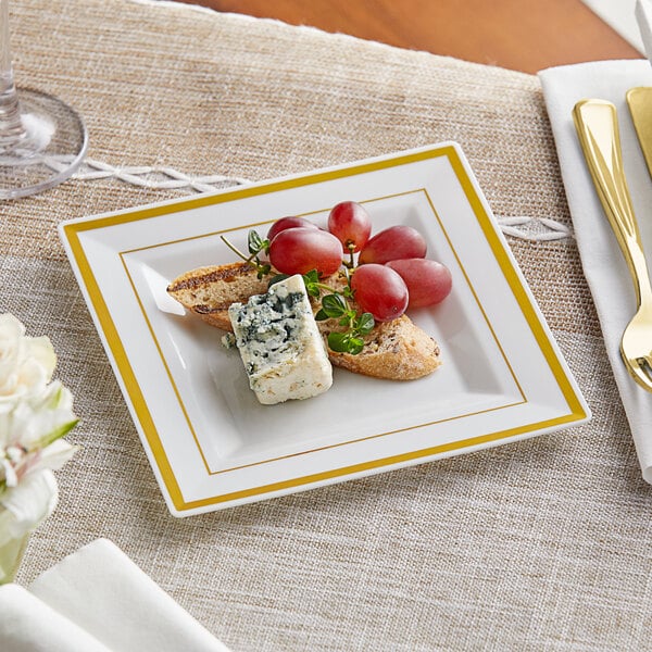 A Visions ivory plastic square plate with gold bands holding cheese and grapes.