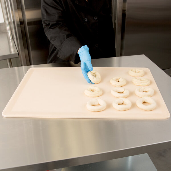 A person in blue gloves placing dough on a MFG Tray fiberglass proofing board.