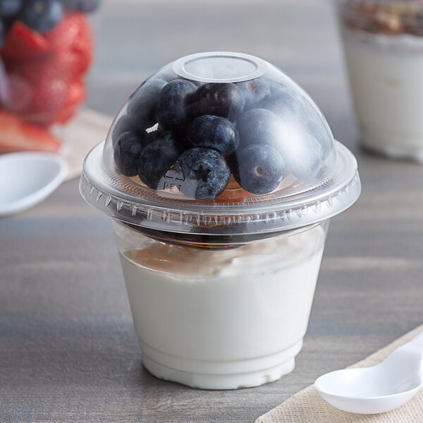 A clear plastic squat cup of yogurt with blueberries and a spoon.