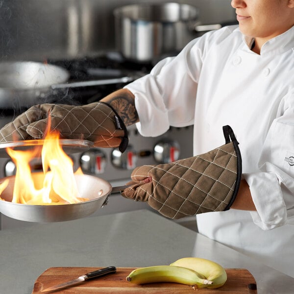 A chef using San Jamar Bestguard oven mitts to hold a pan with fire in it.