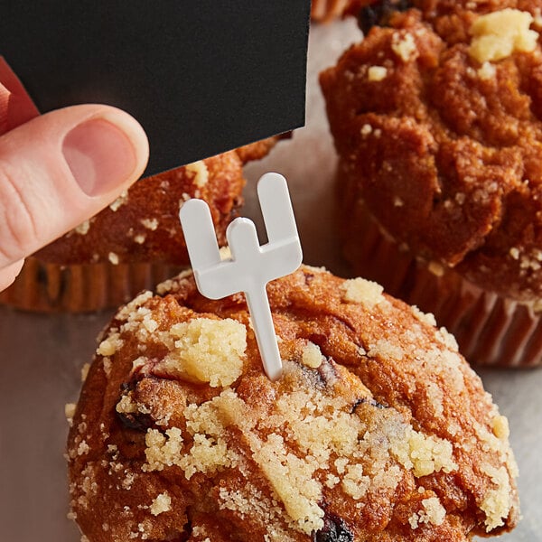 A person holding a white plastic spear in a muffin.