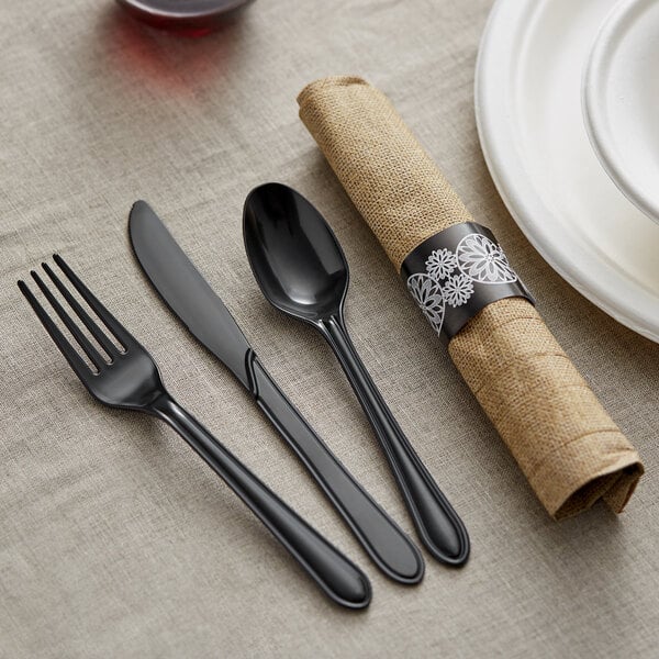A table set with a Hoffmaster FashnPoint burlap print napkin, black plastic silverware, and a black napkin.