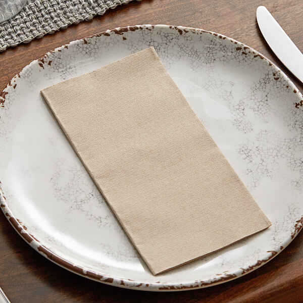 A white plate with a Hoffmaster natural dinner napkin on it.