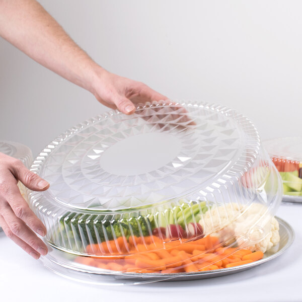 A hand holding a Durable Packaging clear plastic lid over a container of vegetables.