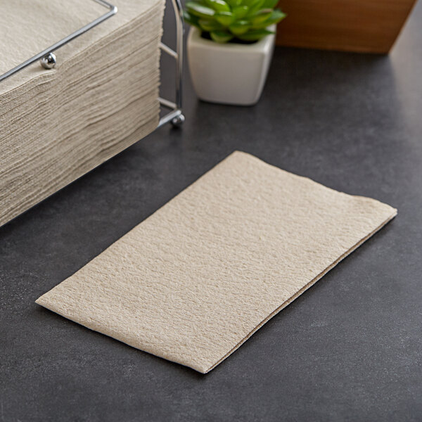 A stack of Hoffmaster Linen-Like Natural Kraft paper guest towels on a table next to a plant.