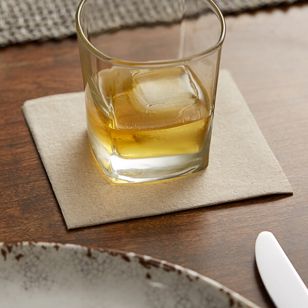 A glass with ice and a drink on a Hoffmaster Linen-Like Natural Kraft beverage napkin.