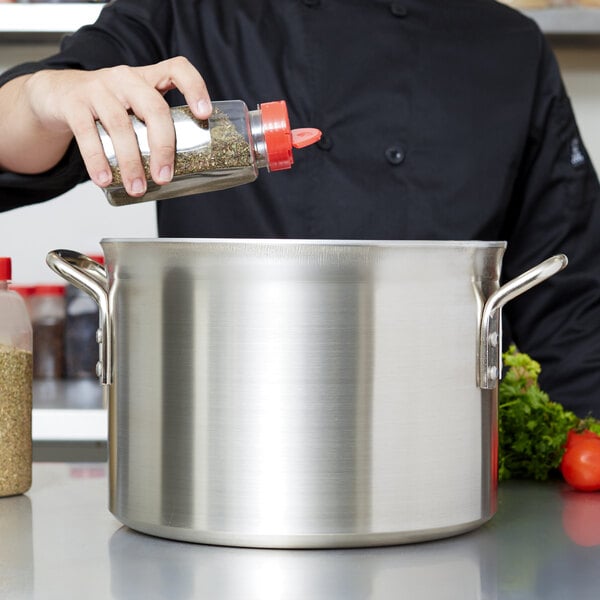 A hand pours seasoning into a Vollrath stainless steel sauce pot.