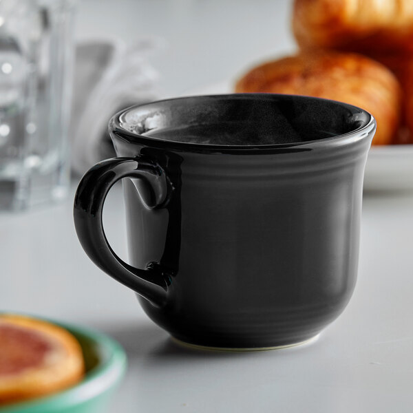 A black Tuxton round china cup with a handle on a table with pastries.