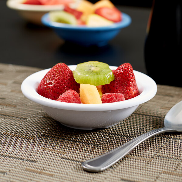 A white Carlisle Kingline melamine bowl filled with fruit on a table with a spoon.