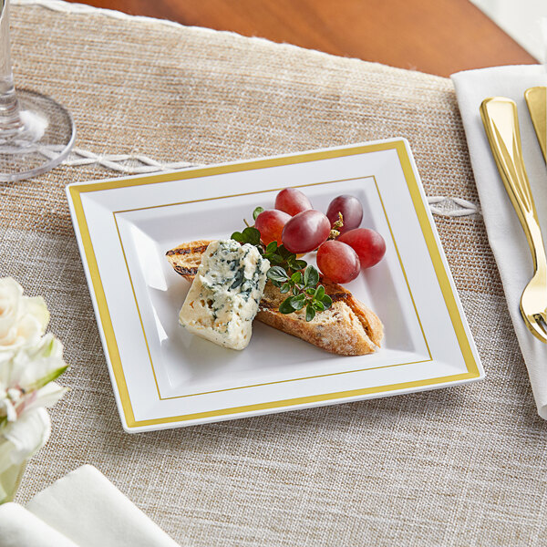 A Visions white plastic plate with gold bands holding grapes and cheese with a piece of bread on a table.