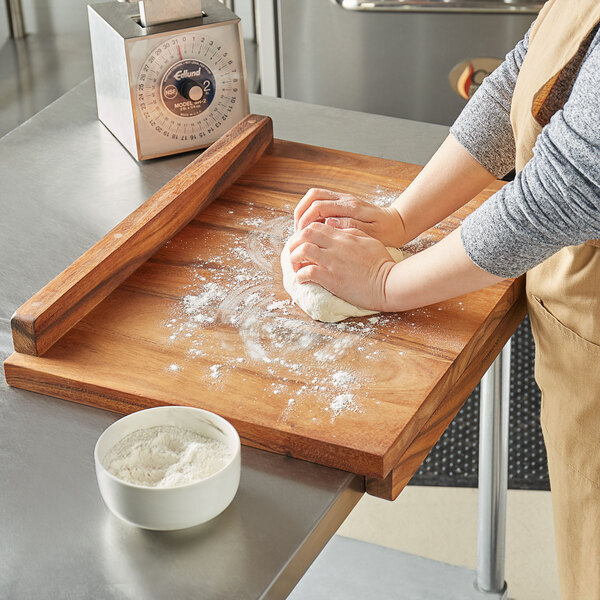 A person kneading dough on a Fox Run wooden pastry board.