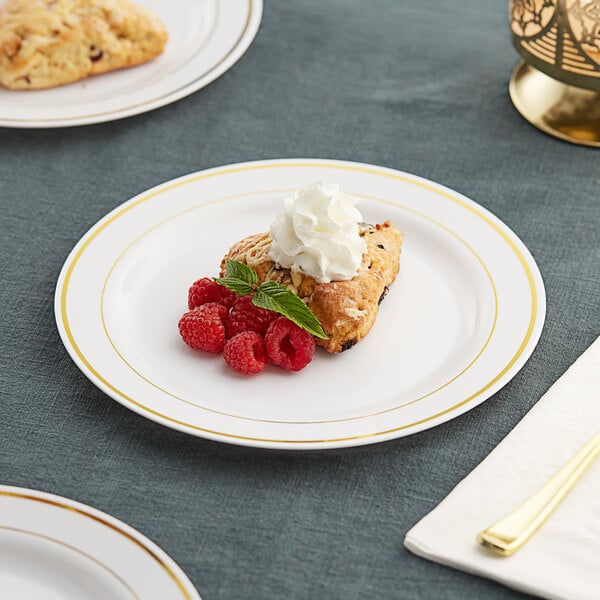 A Visions white plastic plate with gold bands holding dessert with raspberries and whipped cream.