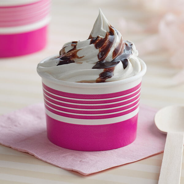A pink paper Choice frozen yogurt cup filled with ice cream and chocolate syrup on a white plate.