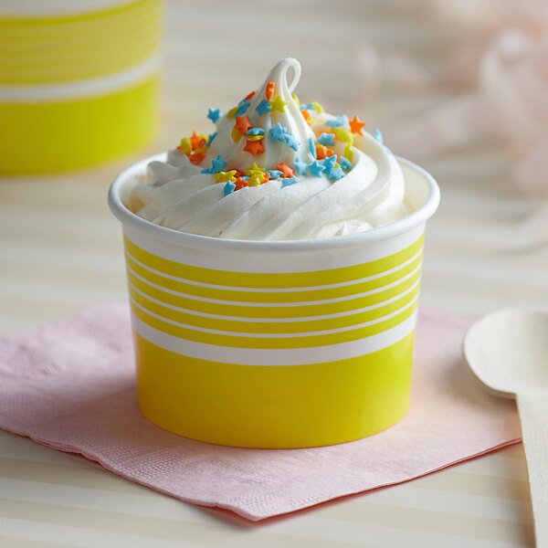 A yellow Choice paper cup filled with ice cream and sprinkles with a spoon.