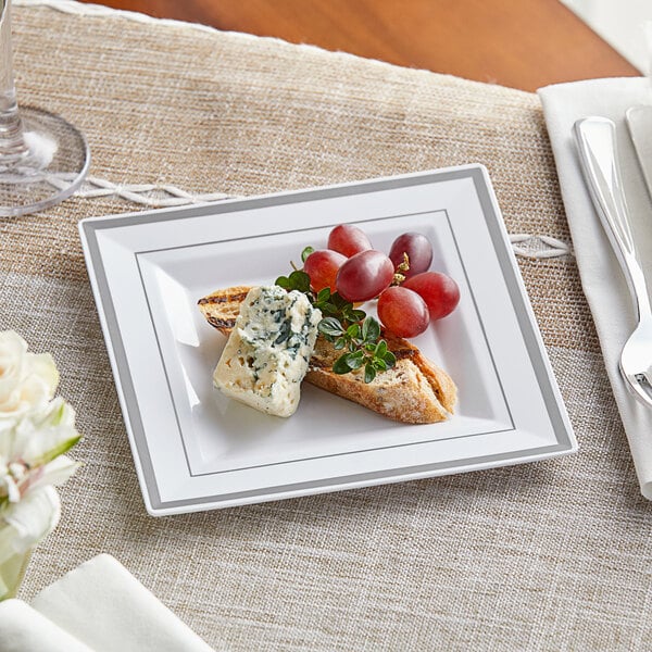 A Visions white plastic plate with silver bands holding grapes and cheese.