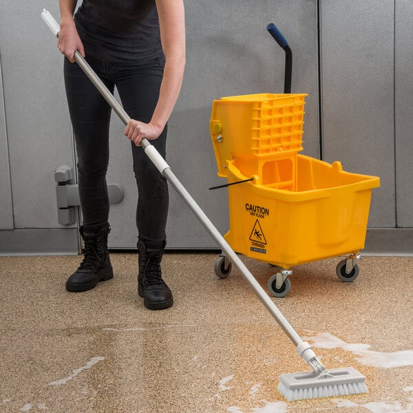 A person using a Carlisle Sparta stainless steel mop handle to clean a floor.