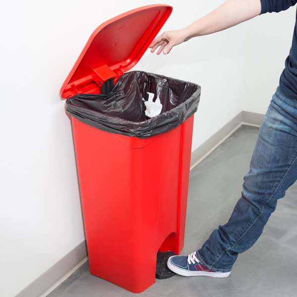 A person reaching to open a red Continental rectangular step-on trash can.