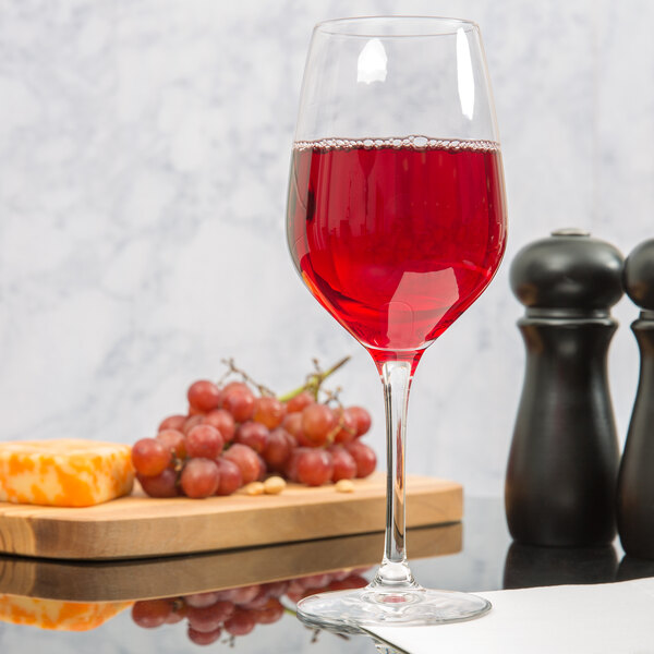 A Stolzle all-purpose wine glass filled with red wine on a table next to a cheese board and grapes.