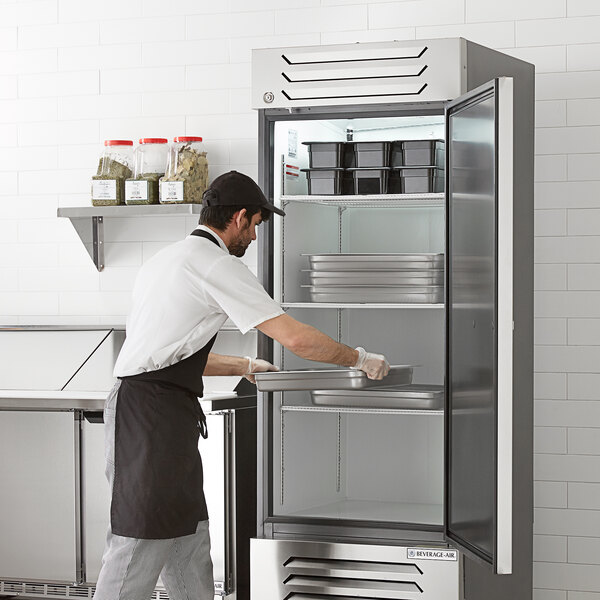 A man in a black apron putting trays in a Beverage-Air Slate Series reach-in refrigerator.