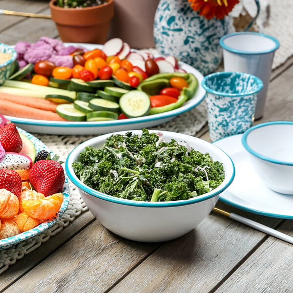 A table with a white enamelware bowl with a turquoise rim filled with kale salad.