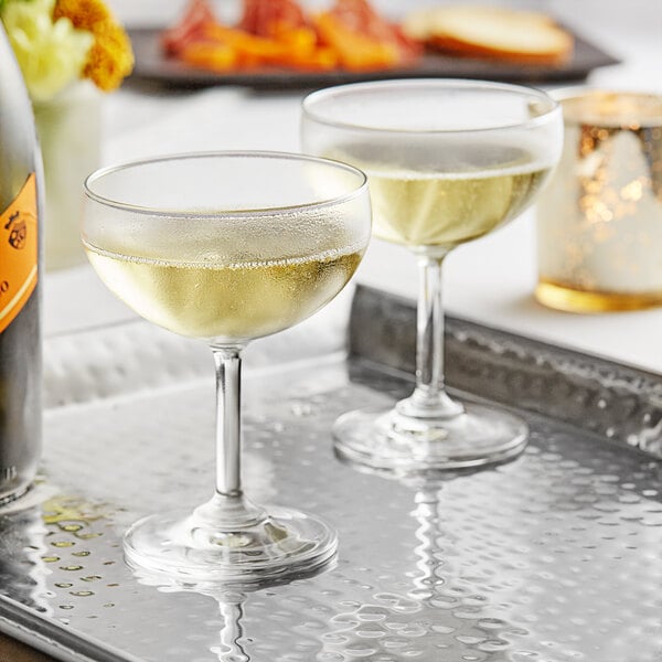 Two Acopa coupe cocktail glasses on a tray with a bottle of champagne.