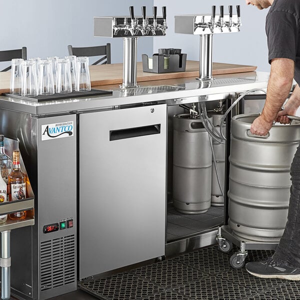 A man standing next to an Avantco stainless steel beer keg dispenser with quadruple taps.