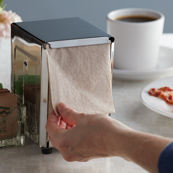 A hand pulling a Choice Kraft Natural Junior low-fold paper towel out of a napkin dispenser.