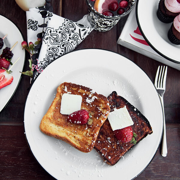 A plate of french toast with strawberries and butter on a Crow Canyon Home enamelware plate with a black rim.